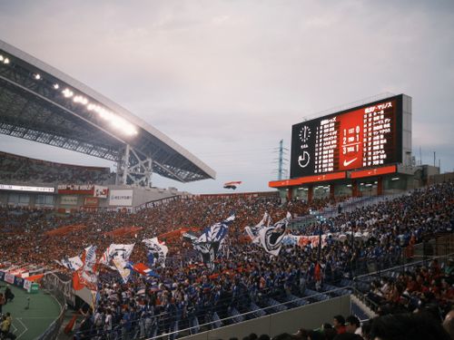 無料 ファンが旗を振り、スコアボードに試合の詳細が表示される、活気のあるサッカー スタジアムのシーン。 写真素材